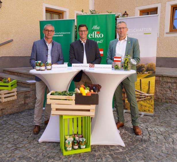 Drei Männer stehen bei einem Infotermin an Stehtischen mit Obst, Gemüse und Gläsern vor Werbebannern.