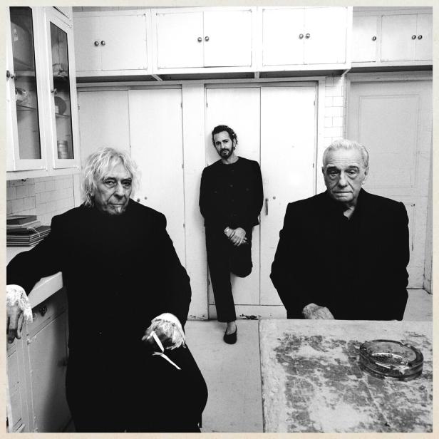 John Cale, Marc Jacobs und Martin Scorsese posieren in Schwarz-Weiß in einer Küche vor weißen Schränken.