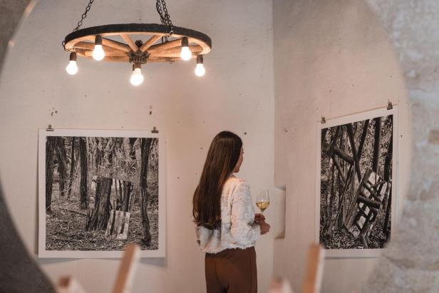 Frau betrachtet Weinbilder in einem Ausstellungsraum und hält ein Glas Weißwein.