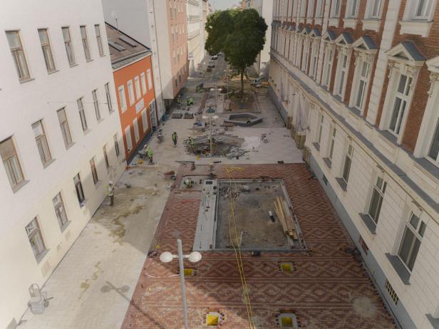 Arbeiter gestalten einen begrünten Stadtplatz mit Baumpflanzungen und Pflasterarbeiten.