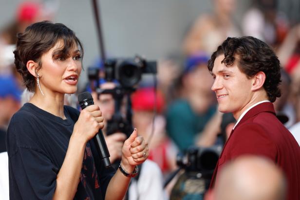 Zendaya spricht mit einem Mikrofon in der Hand neben Tom Holland, der lächelt.