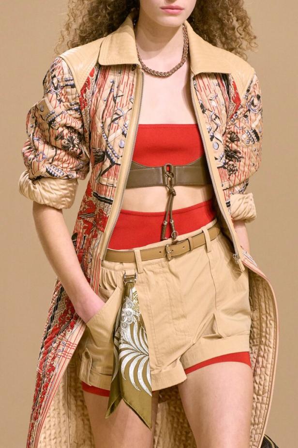 Model trägt gemusterten Mantel, rote Bandeau-Top und Shorts mit Gürteln.