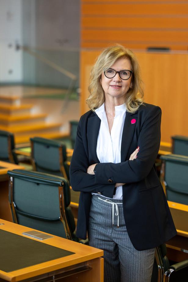 Eine Politikerin steht in einem Sitzungssaal mit verschränkten Armen.