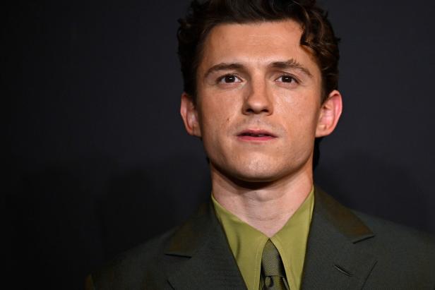 Tom Holland trägt ein olivgrünes Sakko mit einem hellgrünen Hemd vor einem dunklen Hintergrund.