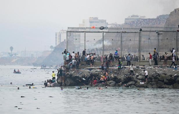 Migrants from Morocco gather by the border fence as they cross the Spanish border, swimming through the sea, as seen from Ceuta