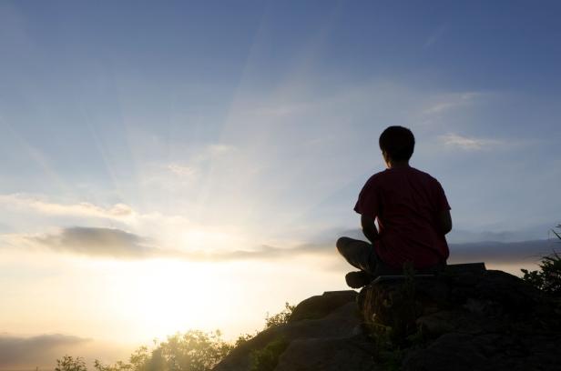 Rear view silhouette of man sitting atop peak at sunset