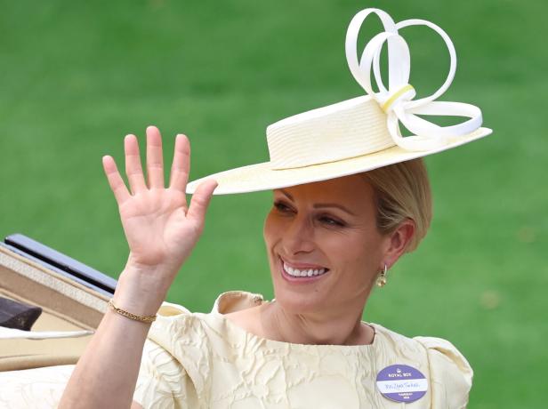 Zara Tindall winkt lächelnd in einem hellgelben Kleid und einem passenden Hut mit auffälliger Schleife.