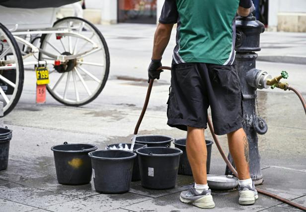 Ein Mann befüllt Kübel an einem Hydranten auf der Straße.