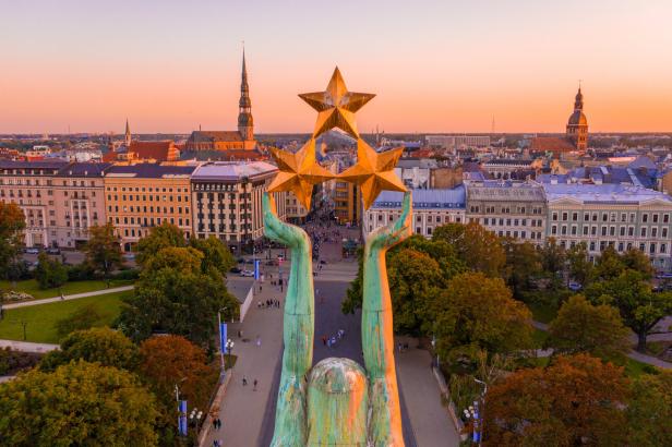 Blick über Riga bei Sonnenuntergang mit dem Freiheitsdenkmal und Sternen darüber.