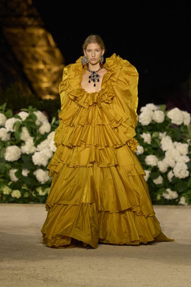 Model in gelbem, mehrlagigem Rüschenkleid mit Schmuck auf dem Laufsteg.