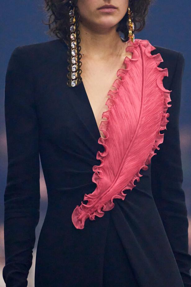 Frau in schwarzem Kleid mit großem pinken Federapplikationsdetail und langen, glitzernden Ohrringen.