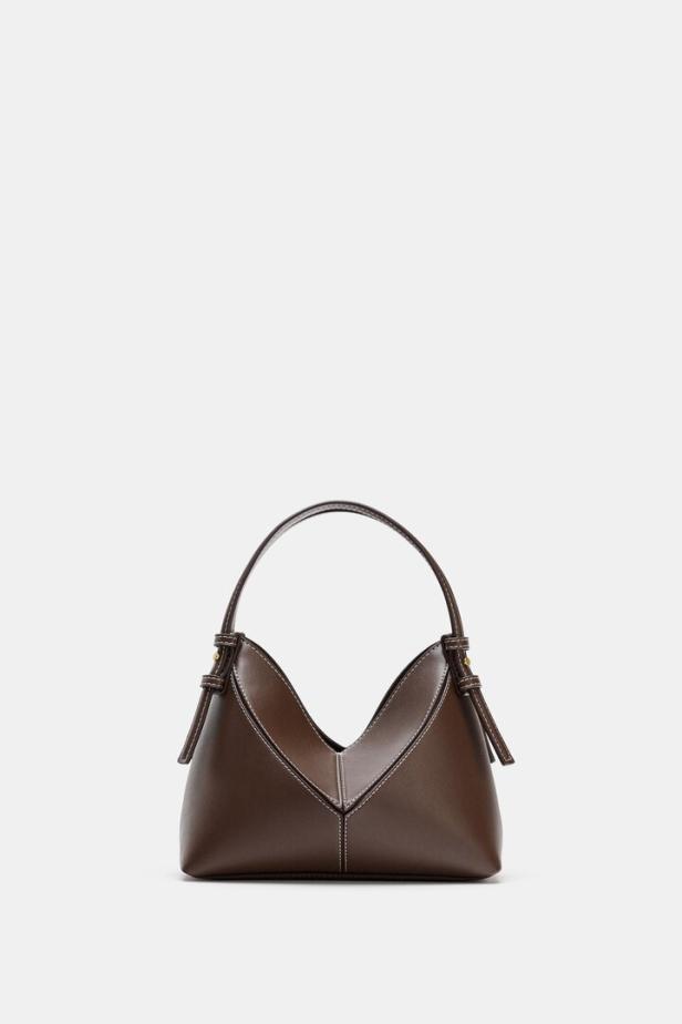 Braune Handtasche mit V-förmiger Vorderseite und kurzem Henkel auf hellem Hintergrund.