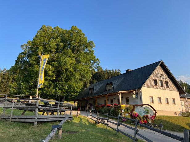 Das Almhaus am Hochbärneck mit wehender Fahne bei wolkenlosem Himmel.