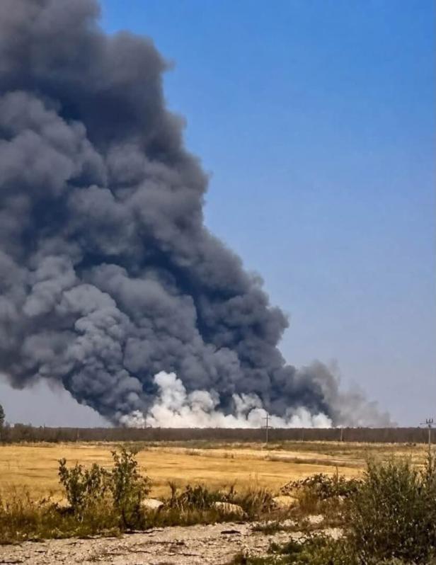 Dicker schwarzer Rauch steigt über einer trockenen Landschaft auf.