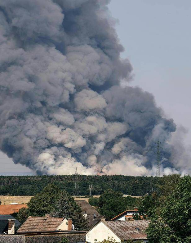 Dichte Rauchwolke steigt hinter einem Dorf auf, vermutlich von einem Brand.