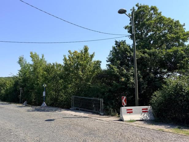Leere Bushaltestelle an einer Straße mit Betonleitwand und Laterne.