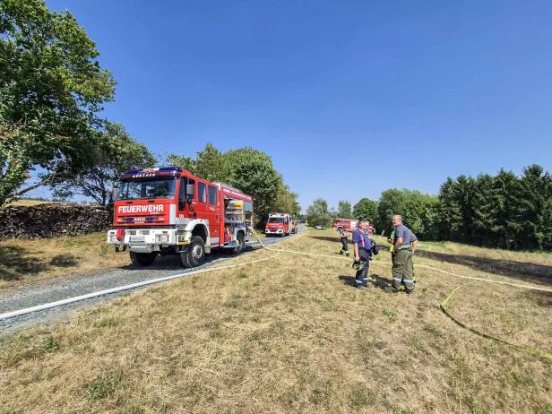 Mehrere Feuerwehrfahrzeuge stehen auf einem Feldweg, während Einsatzkräfte Schläuche verlegen.