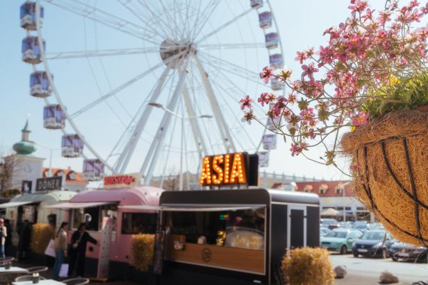 Ein Riesenrad im Hintergrund. Ein asiatischer Foodstand im Vordergrund. 