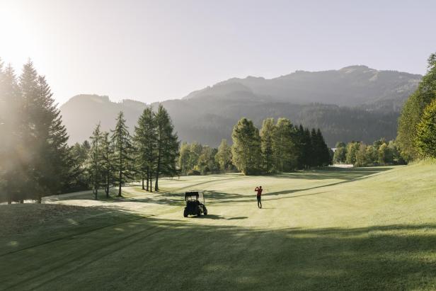 Golfer auf einem sonnigen Platz vor alpiner Bergkulisse.