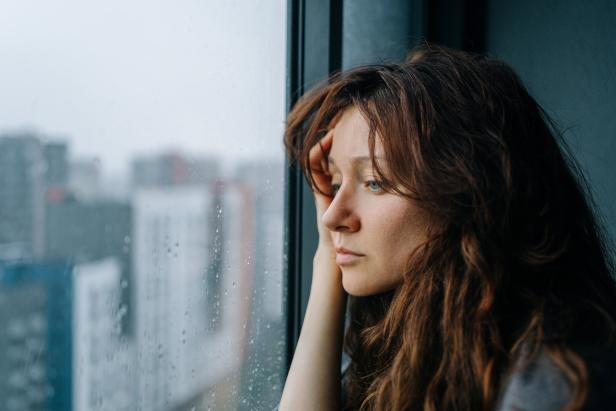 Nachdenkliche Frau mit langem Haar schaut regnerisch aus dem Fenster.