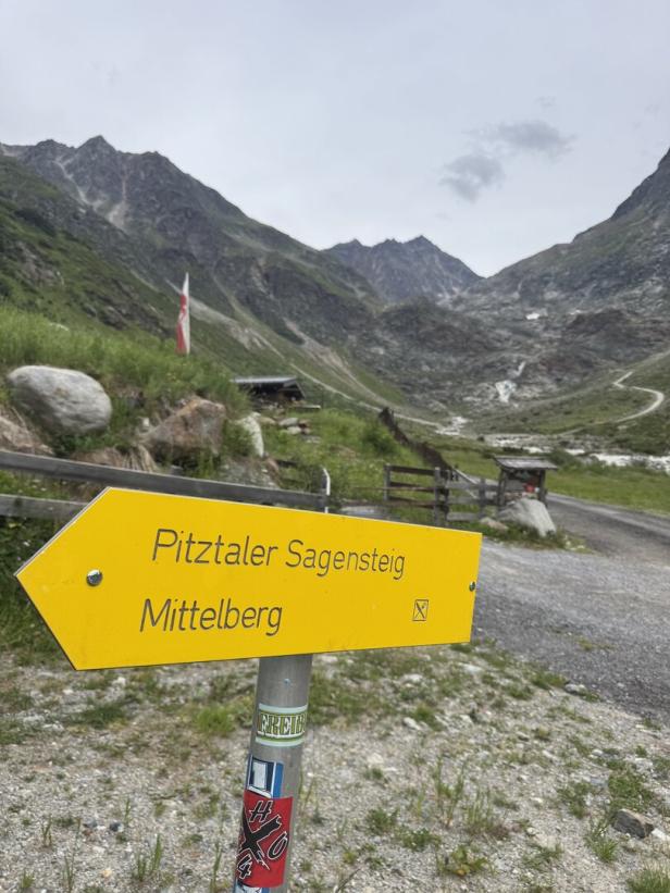 Ein gelber Wegweiser zum Pitztaler Sagensteig und Mittelberg steht vor einer alpinen Berglandschaft.