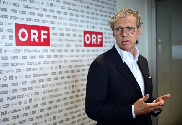 Ein Mann mit Brille und lockigem Haar spricht vor einer Wand mit ORF-Logos.