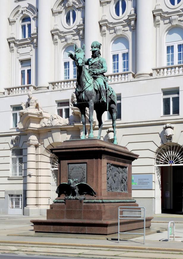 Reiterdenkmal vor einem barocken Regierungsgebäude mit hellen Fassaden und Rundfenstern.