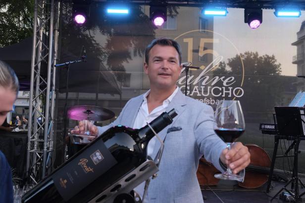 Ein Mann in hellem Sakko hält ein Weinglas mit Rotwein