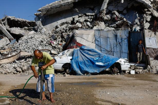 A Palestinian rinses a piece of clothing with water from a hose near rubble from buildings destroyed during the war, at Jabalia refugee camp