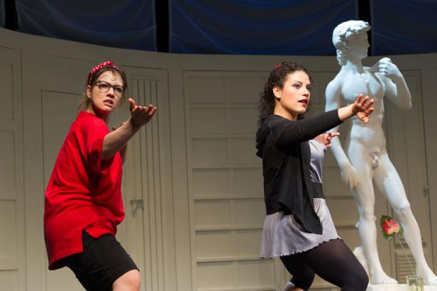 Zwei Schauspielerinnen posieren auf einer Bühne vor einer David-Statue.