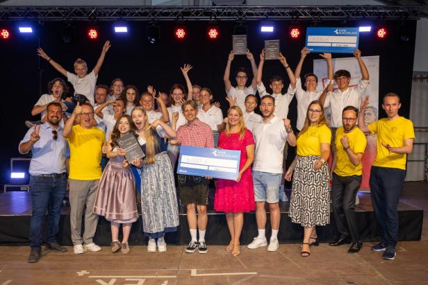 Siegergruppen und Jugendliche posieren auf der Bühne des Golser Volksfests mit Urkunden und Preisgeldschecks.