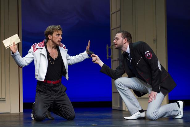 Auf einer Bühne bedroht ein Mann mit einer Pistole einen anderen, der einen Brief in der Hand hält.