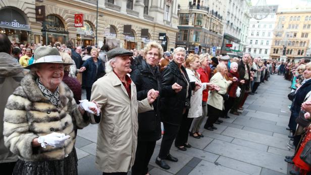 Eine Menschenkette hält Händchen in einer belebten Einkaufsstraße.