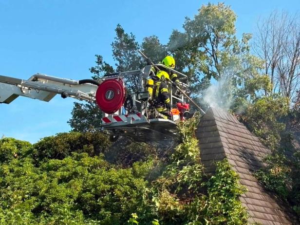 Feuerwehrleute löschen Rauch an einem verwachsenen Dach aus einer Drehleiter.