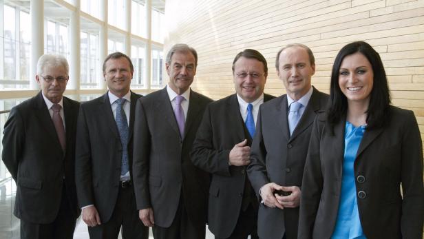 Eine Gruppe von sechs Personen in Anzügen posiert für ein Gruppenfoto.