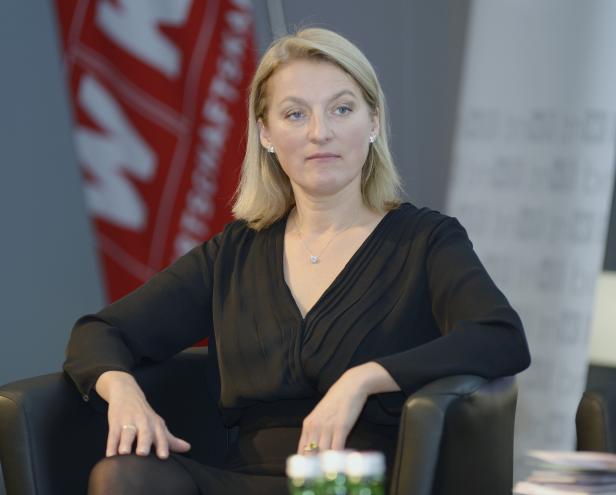 Eine blonde Frau sitzt in einem Sessel und blickt nachdenklich zur Seite.