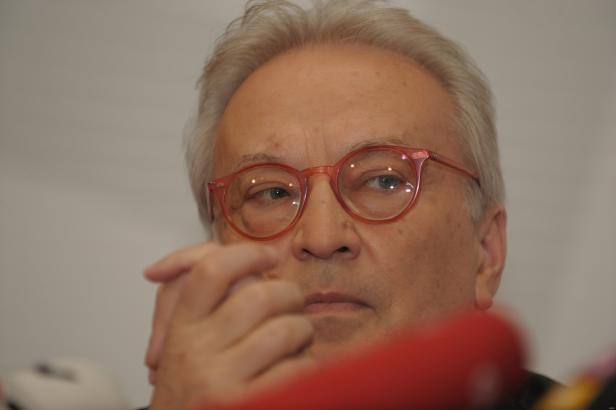 Ein Mann mit hellen Haaren und roten Brillengläsern blickt aufmerksam zur Seite.