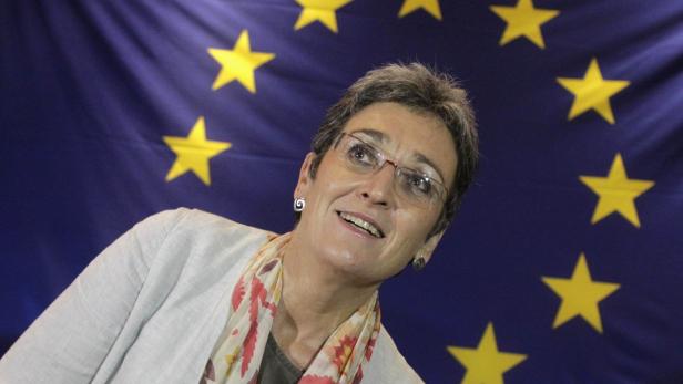 Eine Frau mit Brille lächelt vor der Europaflagge.
