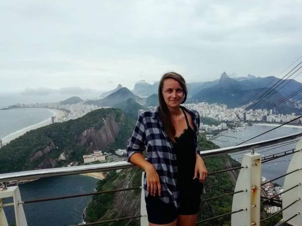Eine Frau steht vor dem Geländer auf dem Zuckerhut in Rio de Janeiro mit Blick auf die Stadt und die Küste.