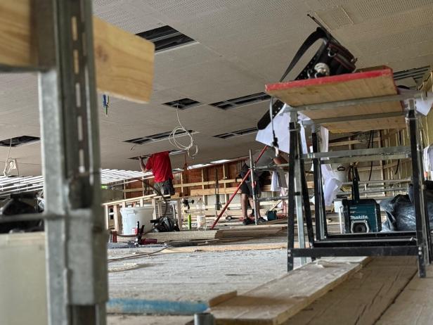 Arbeiter verlegen Deckenplatten in einem Raum im Umbau, umgeben von Gerüsten, Holz und Werkzeugen.