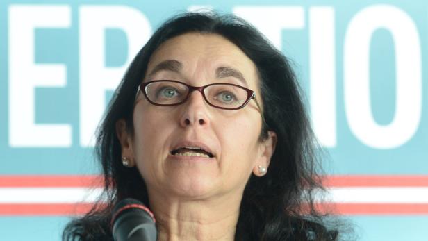 Eine Frau mit Brille spricht in ein Mikrofon vor einem blauen Hintergrund.