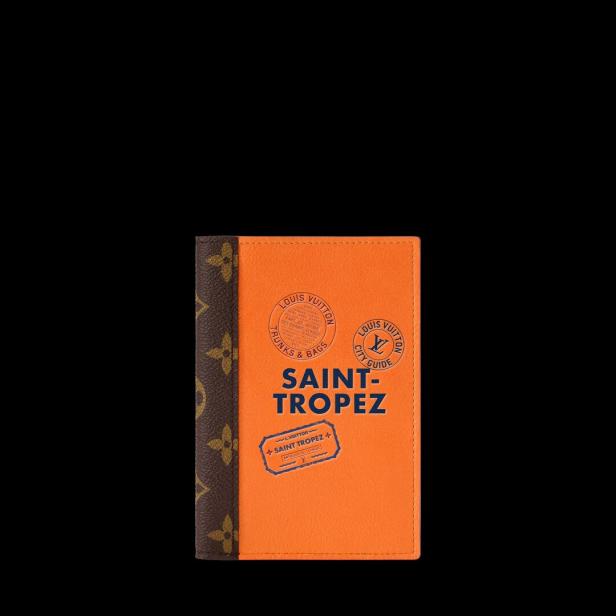 Orangefarbenes Louis-Vuitton-Notizbuch mit „SAINT-TROPEZ“-Aufdruck und dunklem Monogramm-Rücken auf schwarzem Hintergrund.