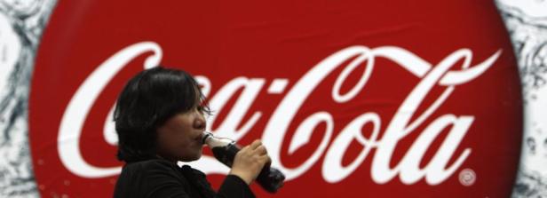 Eine Frau trinkt eine Coca-Cola vor einem großen Coca-Cola-Logo.
