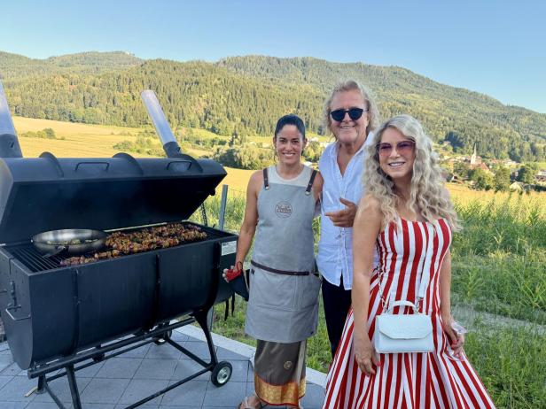 Drei Personen stehen neben einem großen Grill in den Weinbergen.