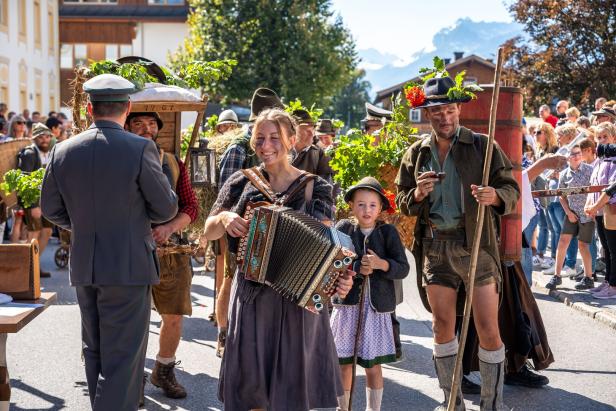 Menschen in traditioneller Tracht bei einem Alpenumzug, vorne eine Frau mit Akkordeon und ein Kind, daneben ein Mann mit Stock.