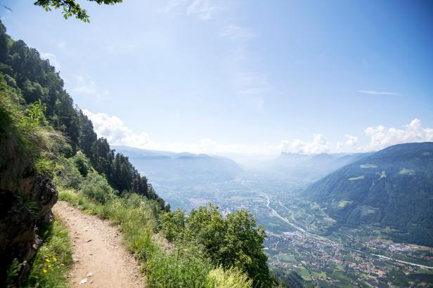 Ein schmaler Wanderweg führt an einem steilen Hang entlang mit Blick auf ein weites Tal und die umliegenden Berge.