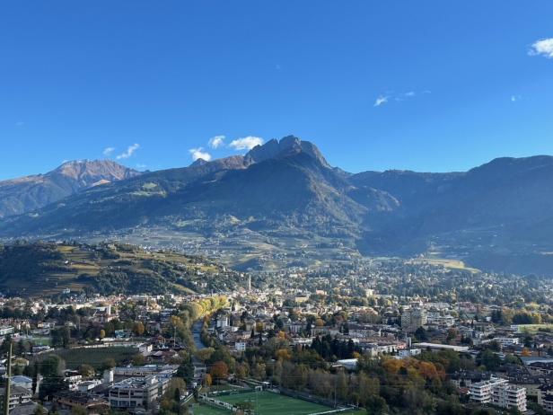 Blick auf die Stadt Meran in Südtirol vor einer imposanten Bergkulisse unter einem klaren blauen Himmel.