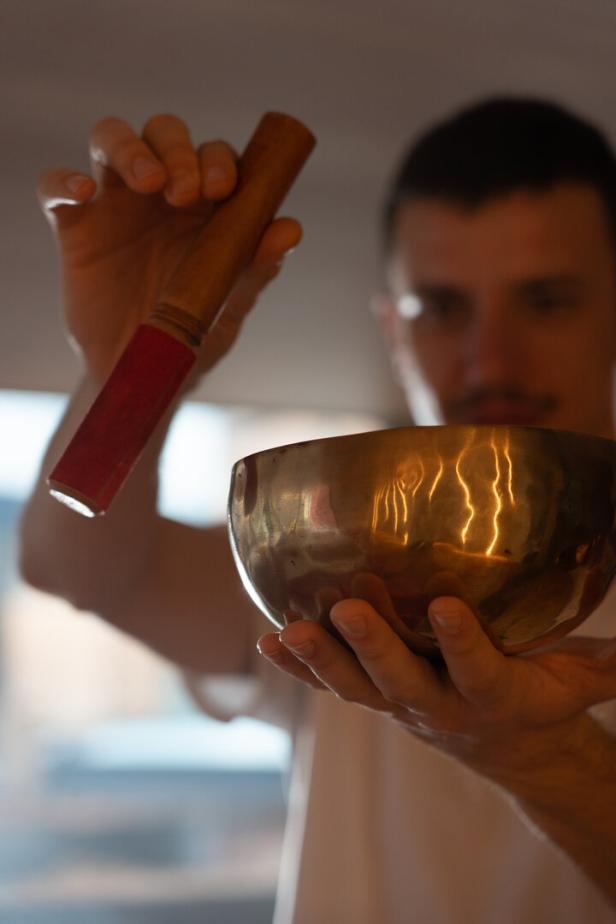 Eine Person hält eine goldene Klangschale in den Händen und bereitet sich darauf vor, sie mit einem Holzklöppel anzuschlagen.