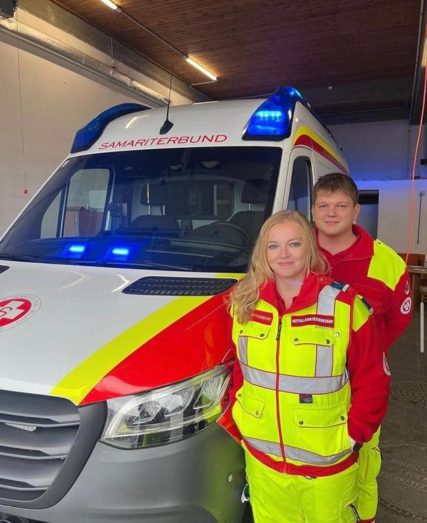 Zwei Sanitäter stehen vor einem Rettungswagen des Samariterbunds mit Blaulicht.