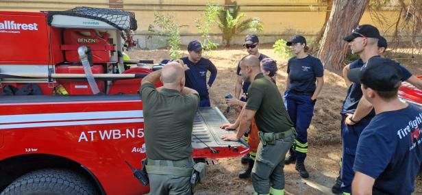 Mehrere Personen in Feuerwehrkleidung stehen rund um die Ladefläche eines roten Einsatzfahrzeugs.
